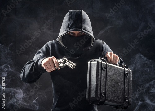 Man in black hoodie with gun and suitcase. Bank robbery. Criminal drug dealer concept.