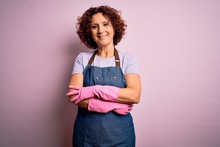 Middle Age Curly Hair Woman Cleaning Doing Housework Wearing Apron And Gloves Happy Face Smiling With Crossed Arms Looking At The Camera. Positive Person.