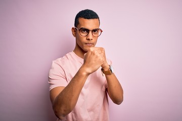 Handsome african american man wearing casual t-shirt and glasses over pink background Ready to fight with fist defense gesture, angry and upset face, afraid of problem