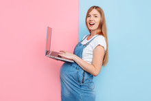Photo Of A Cheerful Pregnant Woman Using A Laptop Computer, Standing On An Isolated Pink And Blue Background