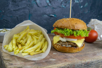 Wall Mural - Close-up hamburger on a wooden board, near are fries, tomatoes and sauce