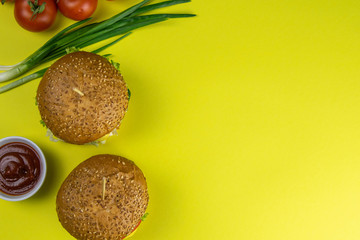 Wall Mural - Hamburgers close-up on a yellow background, next are sauces and tomatoes with green onions