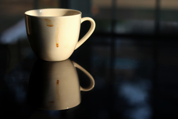 Coffee cup white color empty and dirty after drinking on the glass table. Reflection shadow of Coffee cup.