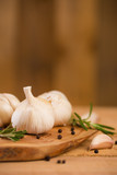 Fototapeta Miasto - Fresh garlic with spices on a wooden background, thyme and rosemary. Culinary background, ingredients for marinade, close up. Vertical frame