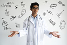 Confused Doctor In Lab Coat With Hand Drawn Medical Sketches. Serious Indifferent Young Clinical Worker With Stethoscope On Neck Shrugging Shoulders And Looking At Camera. Puzzlement Concept