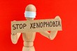Cardboard sign with text stop xenophobia in the hands of a wooden doll or mannequin in a medical mask. Concept of anti racism, anti xenophobia, the social situation around the Coronavirus or Covid-19.