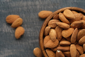 Wall Mural - Almonds nuts close-up  on a wooden brown scratched background.Raw almonds in a round wooden cup on a black slate background.Vegetarian and vegan food.Healthy food.