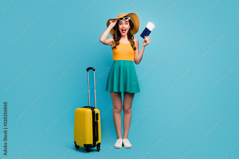 Full body photo of pretty lady traveler hold passport tickets rolling suitcase luggage airport cheap flights wear sun specs short summer dress headwear shoes isolated blue background - obrazy, fototapety, plakaty 