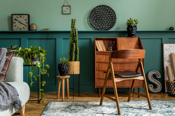 Modern and retro composition of home office interior with wooden cabinet, chair, plants, decoration and elegant personal accessories. Stylish vintage concept of home decor. Wood panelling. Template.