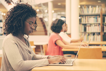 Wall Mural - focused female customer using public wi-fi hotspot in library. young african american woman sitting 