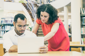 Wall Mural - instructor helping trainee with project in library. man and woman in casual sitting and standing at 