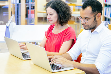 Wall Mural - serious adult students taking exam in classroom. man and woman in casual sitting at desk, using lapt