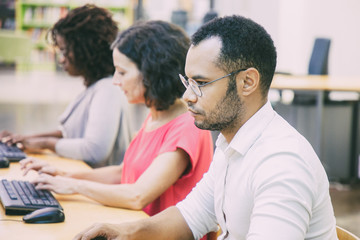 Wall Mural - serious adult male student studying in computer class. row of man and women in casual sitting at tab