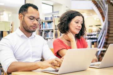 Wall Mural - adult college students discussing project while working on computers in library. man and woman in ca