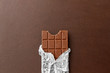 sweets, confectionery and food concept - milk chocolate bar in foil wrapper on brown background