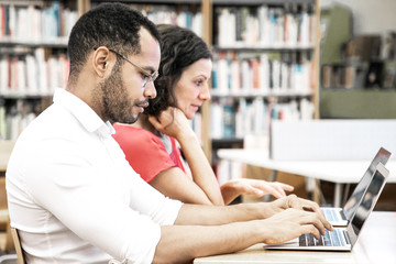 Wall Mural - College students working in library computer class. Man and woman in casual sitting at desk, using laptops, typing. Library computer class concept