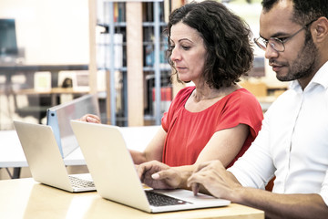 Wall Mural - focused adult students taking tests in classroom. man and woman in casual sitting at desk, using lap