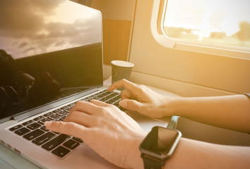 Selective focus of woman hand which she is a freelance working with laptop in the train and a coffee cup in the morning