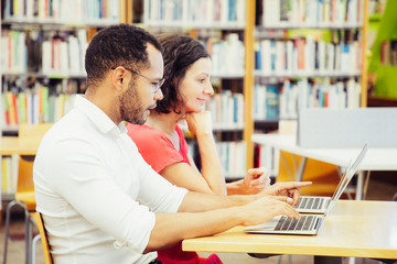 Wall Mural - positive excited students enjoying webinar in library. man and woman in casual sitting at desk with 