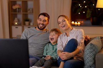 Poster - family, leisure and people concept - happy smiling father, mother and little son with remote control watching tv at home at night