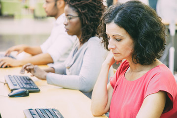 Wall Mural - pensive middle aged female student working in computer class. line of man and women in casual sittin