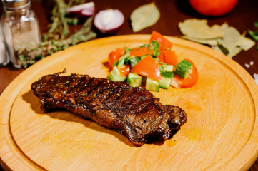 A juicy piece of fried meat lies on a cutting board against a wooden table.