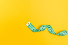 Green Plastic Measuring Tape On A Yellow Background. Diet, Slimming, Obesity Concept.