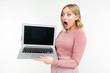 © Ivan Traimak - surprised blonde girl in pink clothes holds a laptop with the display forward with an empty blank on a white studio background