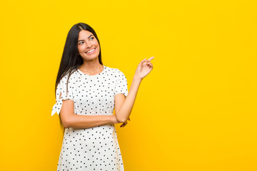 Wall Mural - young pretty latin woman smiling happily and looking sideways, wondering, thinking or having an idea against flat wall