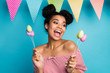 Photo of pretty dark skin lady hold holiday painted eggs on stick colorful decor flags good mood family meeting wear red white striped shirt naked shoulders isolated blue color background