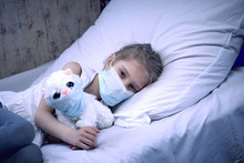 A Girl With White Hair In A Medical Mask On Her Face. Nearby, A Soft Toy On Her Face Is Also A Cough Mask. Close-up