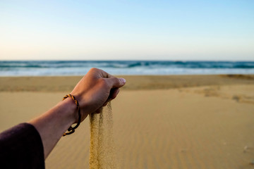 A hand strews sand on the beach in front of the evening see