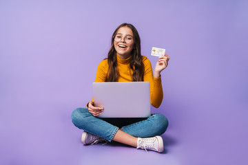 Wall Mural - Image of young woman holding credit card and using laptop while sitting