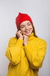 © Mangostar - Happy young woman in red knitted hat. Portrait of beautiful young woman in yellow sweater and red hat standing with closed eyes isolated on white background. Happiness and style concept