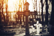 A Beautiful Old Rusty Cross Stands In A Large Dark Cemetery Against A Background Of White Crosses And Tree Trunks, Illuminated By Bright Sunlight.