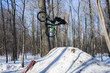 Mountainbikerider does a backflip on a bike in winter. An athlete in a helmet on dirt jumping does the trick in snowy weather. Winter bike trick