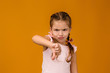 © producer - Cute little child girl in dress showing the thumbs down gesture on yellow background.