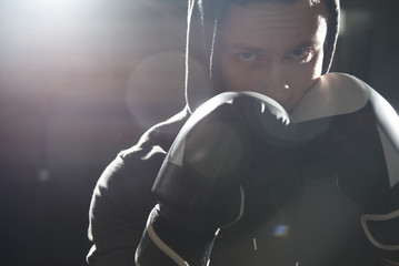 Wall Mural - Closeup portrait of a cool professional boxer in gloves and a hood, aggressively looking at the camera, beating with his fist