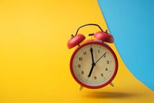 Red Retro Alarm Clock Floating In The Air With Yellow And Blue Background.