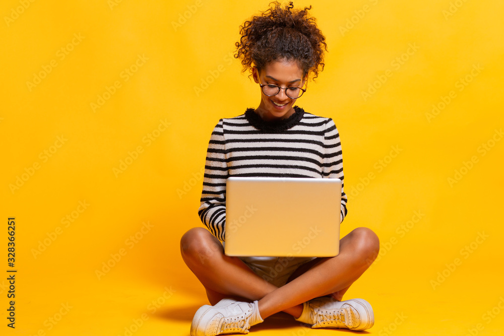 Smiling african woman using laptop computer while sitting looking aside. Copy space. Not isolated. - obrazy, fototapety, plakaty 