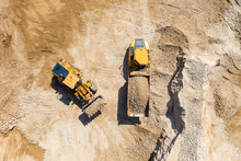Bucket Loader Loading Gravel Onto An Articulated Hauler Truck Trailer At A Large Construction Site, Top Down Aerial View.