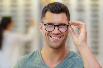 handsome man choosing glasses in optics store