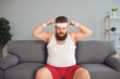 © Studio Romantic - Funny fat man in sportswear is sitting on the sofa in the room