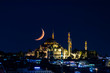 The moon stands like a crescent moon over the Fatih Mosque at night