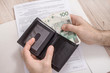 Deklaracja podatkowa leży na stole. Męskie dłonie wyjmują z portfela banknoty w walucie PLN. Podatek do zapłaty. 