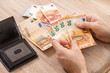 Męskie dłonie układają na stole banknoty Euro. Czarny skórzany portfel leży na stole.