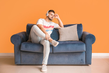 Sticker - Young man listening to music while sitting on sofa at home