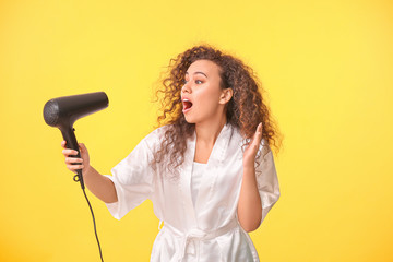 Wall Mural - Beautiful surprised African-American woman with blow dryer on color background