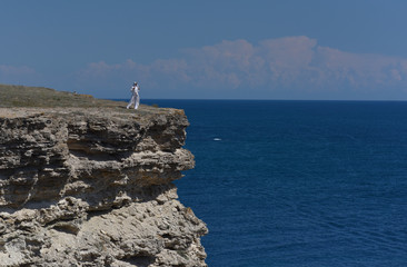 Wall Mural - a girl in white clothes stands on the edge of a cliff above the sea