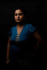 portrait of a beautiful Indian Bengali brunette woman in light and shadow before a black copy space background wearing a blue top. Indian lifestyle and fashion  portrait